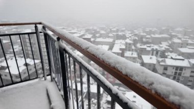 Kar zemini ve çatıları kaplıyor. Balkondan şehir manzarası var..