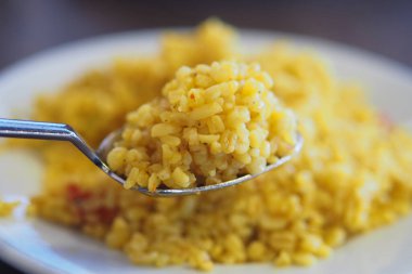 Bir kaşık altın pirinci daha fazla pirinçle dolu bir tabağın üzerinde tutar..