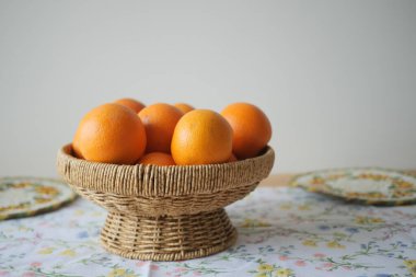 Bir sepet taze portakalları çiçekli bir bezle bir masada tutar..