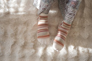 İki ayaklı renkli çoraplar içinde parlak bir odada yumuşak bir halıya oturmuş..