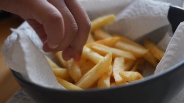 Bir el masaya yerleştirilmiş bir kasede kızarmış patates kızartmasına uzanır..