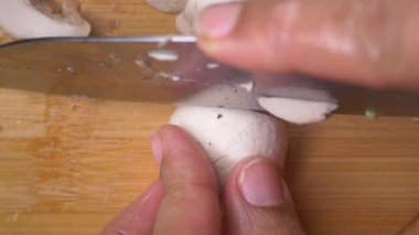 Kullanıcı mutfaktaki tahta bir tahtada mantar kesiyor..