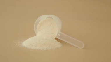 Süt tozu bir yüzeyde plastik kepçeyle gösterilir..