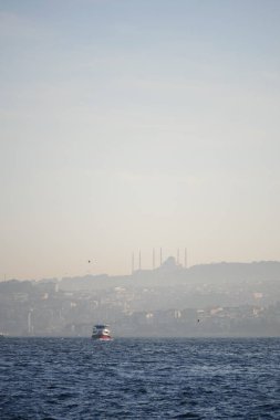 Bir feribot, alacakaranlıkta arka planda bir şehirle birlikte su üzerinde hareket eder..