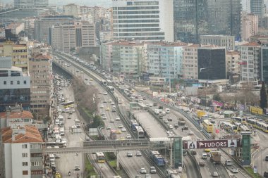 Arka planda binalar yükselirken arabalar ve otobüsler yolu dolduruyor..