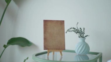 Kağıt, arka planda vazo ve bitki ile sehpanın üzerinde duruyor..