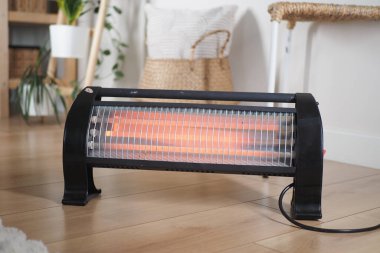 Sıcak bir odada, yumuşak ışıklandırmalı ısıtıcı kullanan bir insan..