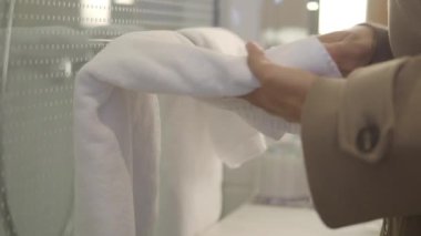 Bir insan otel banyosundaki lavabonun yanında havlu katlar..