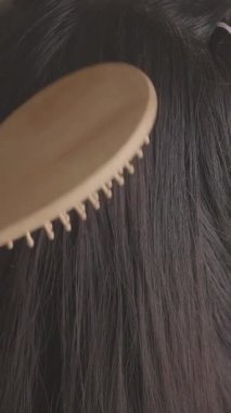 Bir kişi uzun saçlarını ahşap bir saç fırçasıyla tarıyor..