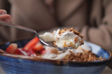 Bir insan kahvaltıda yoğurt, tahıl ve meyve yiyor..
