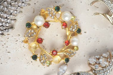 Yüzeyde kırmızı, yeşil ve beyaz taşlı küçük yuvarlak broş gösteriliyor..