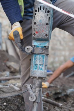 Bir işçi dışarıda inşaat yaparken bir kaya matkabı kullanıyor..