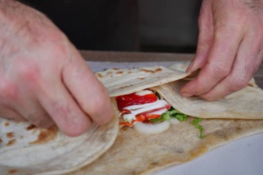 Bir insan içine sebze ve sos ekleyerek bir paket hazırlar..