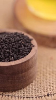 Çuval bezi yüzeyindeki ahşap bir kasede siyah kimyon tohumları.