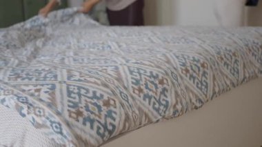 Bir insan odadaki bir yatakta çarşafları düzleştiriyor..