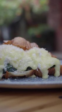 Bir kruvasan, üzerinde erimiş peynir ve ıspanak olan bir tabakta oturur..