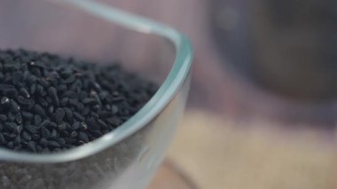 Ahşap bir yüzeyde cam bir kasede siyah kimyon tohumları..