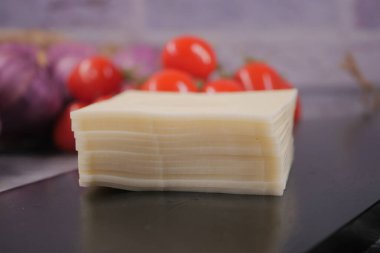 Peynir dilimleri arka planda kırmızı domateslerle siyah bir masaya istiflenir..