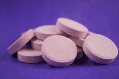 Birkaç pembe tablet mor arka planda istiflenmiş ve dağınık..