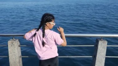 Bir çocuk suyun kenarında durur ve iskelede dalgaları izler..