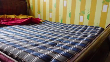 Kareli battaniyeli bir yatak sarı duvarlı bir odada oturur..