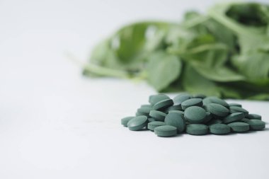 Yeşil tabletler beyaz bir yüzeyde, taze yeşil yaprakların yanında..