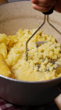 Bir insan ezici kullanarak haşlanmış patatesleri metal bir kasede ezer..