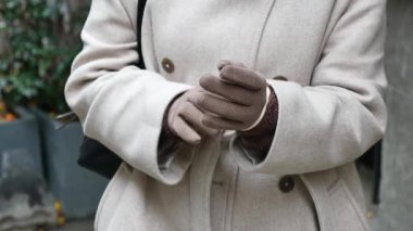 Bir kadın şehir içinde yürürken eldivenlerini düzeltiyor..