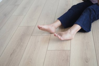 Kişi tahta zemine oturur, çıplak ayakla yüzeye dokunur, rahatlar..