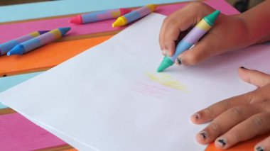 Bir çocuk, masaya konan beyaz kağıda boya sürmek için boya kalemleri kullanır..
