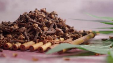 Karanfiller ahşap bir yüzeyde, tarçın çubukları ve yapraklarının yanında otururlar..