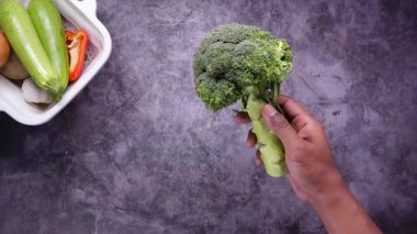Elleri taze brokoliyi renkli sebzelerle dolu bir masanın üstünde tutuyor..