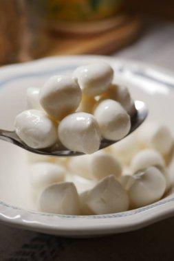 Bir kaşık küçük beyaz peynir toplarını kasenin üstünde tutar..