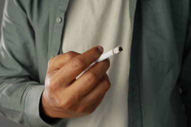 Bir elinde yanan bir sigarayla odanın içinde duran bir insan..