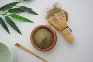 Yeşil çay tozu bambu çırpıcısının ve yaprakların yanında bir kasede duruyor..