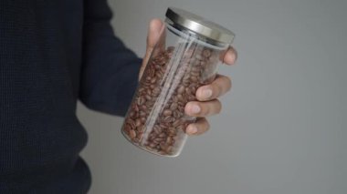 Bir insan elinde kahve çekirdeği dolu cam bir kavanoz tutar..