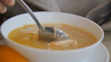 Ev mutfağında bir kase tavuk çorbasını taze malzemelerle karıştıran biri..