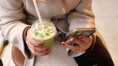 Kafede oturan bir kadın elinde içkiyle telefonunu kontrol ediyor..