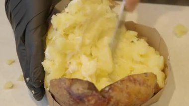 Bir insan fırında patates keser ve tereyağı ve ekşi krema ekler..