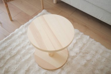 Yuvarlak ahşap bir masa oturma odasındaki tüylü bir halıya oturur..