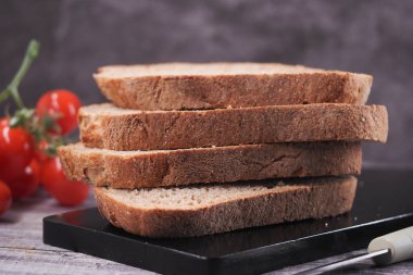 Çeri domatesli, siyah bir tahta üzerinde tam tahıllı ekmek dilimleri..