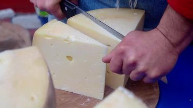 Pazarda biri peyniri parçalara ayırıyor. Dekor hareketli ve renkli..