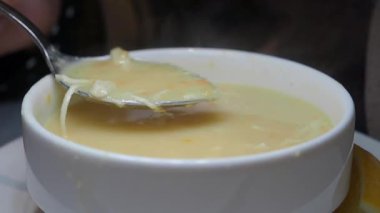 Bir insan beyaz bir kaseden bir kaşık sıcak çorba kaldırır..