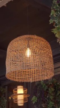 Yakınlarda bitkileri olan bir kafedeki masanın üzerinde örülmüş bir lamba var..