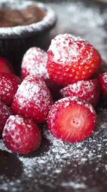 Taze çilekler pudra şekerli siyah bir tabağa konur..