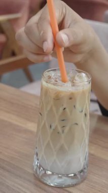 Kafe ortamında pipetle buzlu kahve karıştırır..