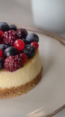 Çeşitli böğürtlenlerle kaplı bir cheesecake ve arka planda bir kahve fincanı..