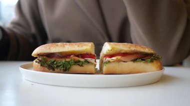 Bir insan ekmek, et ve sebze kullanarak sandviç hazırlar..