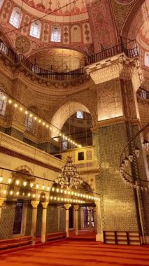 İnsanlar ışık ve dekoratif duvarlarla dolu bir caminin içinde yürüyorlar..