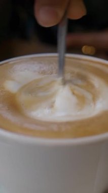 Bir insan sabahları yerel bir kafede kremayı sıcak kahveye karıştırıyor..